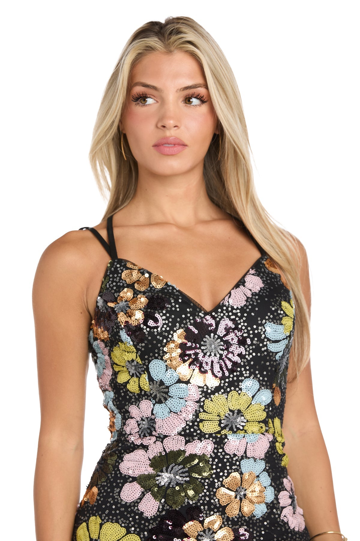 A woman with long blonde hair wears the Floral-Sequin Long Black Prom Dress: Morgan 19051, a black gown decorated with large, colorful floral sequins. She gazes slightly left with a neutral expression.